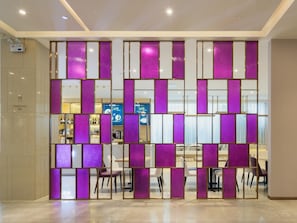 Eine Hotelhalle mit modernem Design, inklusive einer Trennwand mit violetten Paneelen und einem Empfangstresen im Hintergrund.