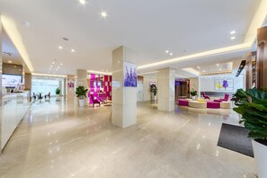 A modern hotel lobby with a reception desk, seating areas, and a reception counter.