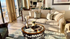 A living room with a beige sofa, a round coffee table with a decorative bowl, and a view of the outdoors through large windows.