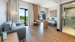 Una habitación de hotel moderna con sofá, escritorio con televisor, cama y zona de ducha de vidrio.