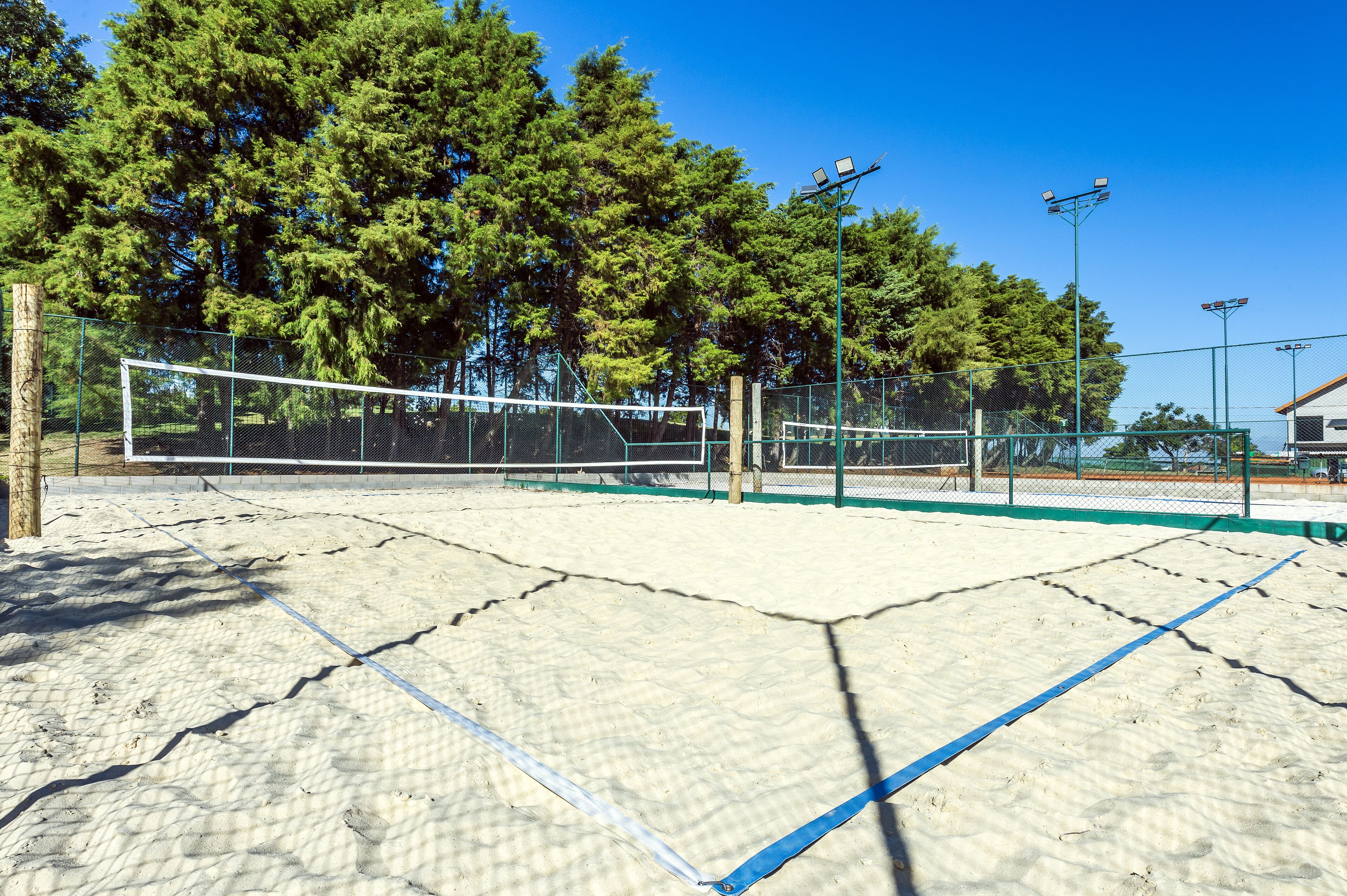 An outdoor tennis court with a net, surrounded by a fence and trees.