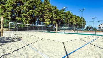 An outdoor tennis court with a net, surrounded by a fence and trees.