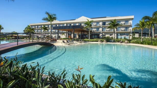 Un resort con una piscina grande, palmeras y un edificio con varios balcones.