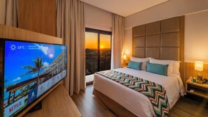 Una habitación de hotel con una cama, un televisor y vistas a la puesta de sol por la ventana.