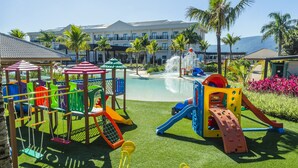 Zona de juegos infantiles con toboganes y columpios, piscina y palmeras.