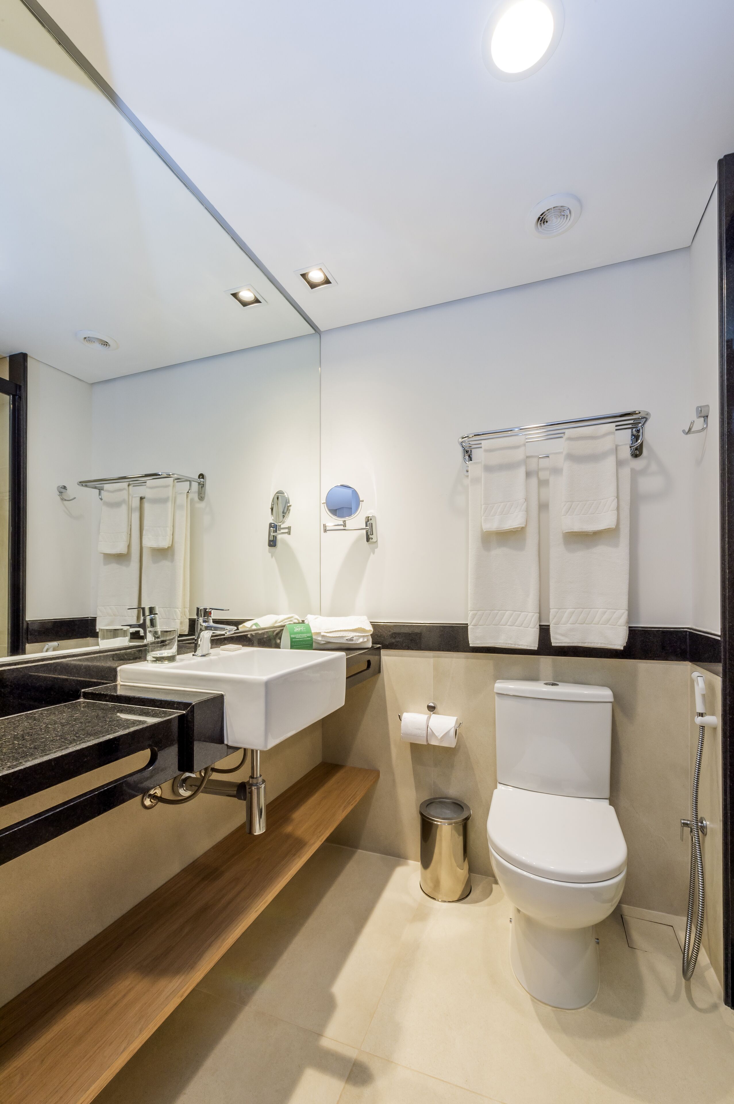 Un baño moderno con lavamanos, espejo, toallero, inodoro y ducha.