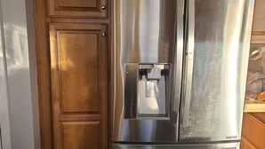 Un refrigerador de acero inoxidable con dispensador de agua, frente a muebles de cocina de madera.
