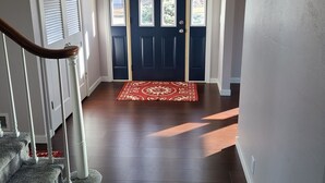 Una escalera conduce a una puerta azul oscuro con tres ventanas, un tapete rojo estampado y un ventilador de techo.