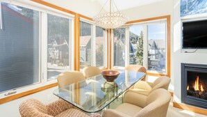 Una sala de estar moderna con una mesa de comedor de vidrio, sofás color beige, ventanas amplias y una chimenea.