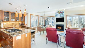 Una cocina moderna con encimeras de granito, armarios de madera y una isla central. Hay un comedor con sillas rojas y una chimenea.