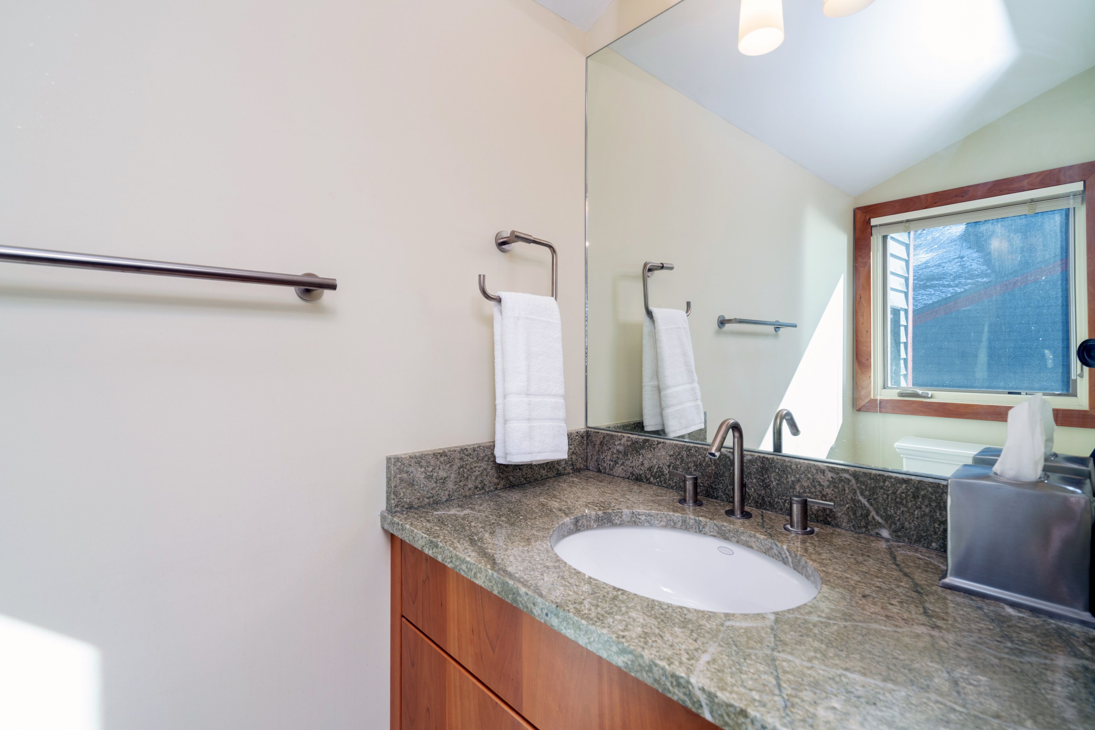 A bathroom with a granite countertop, a white sink, a mirror, and a towel rack.