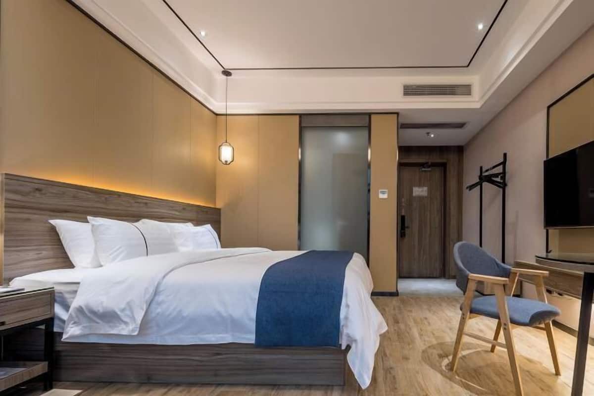 A modern hotel room with a bed, a desk, a chair, and a television.