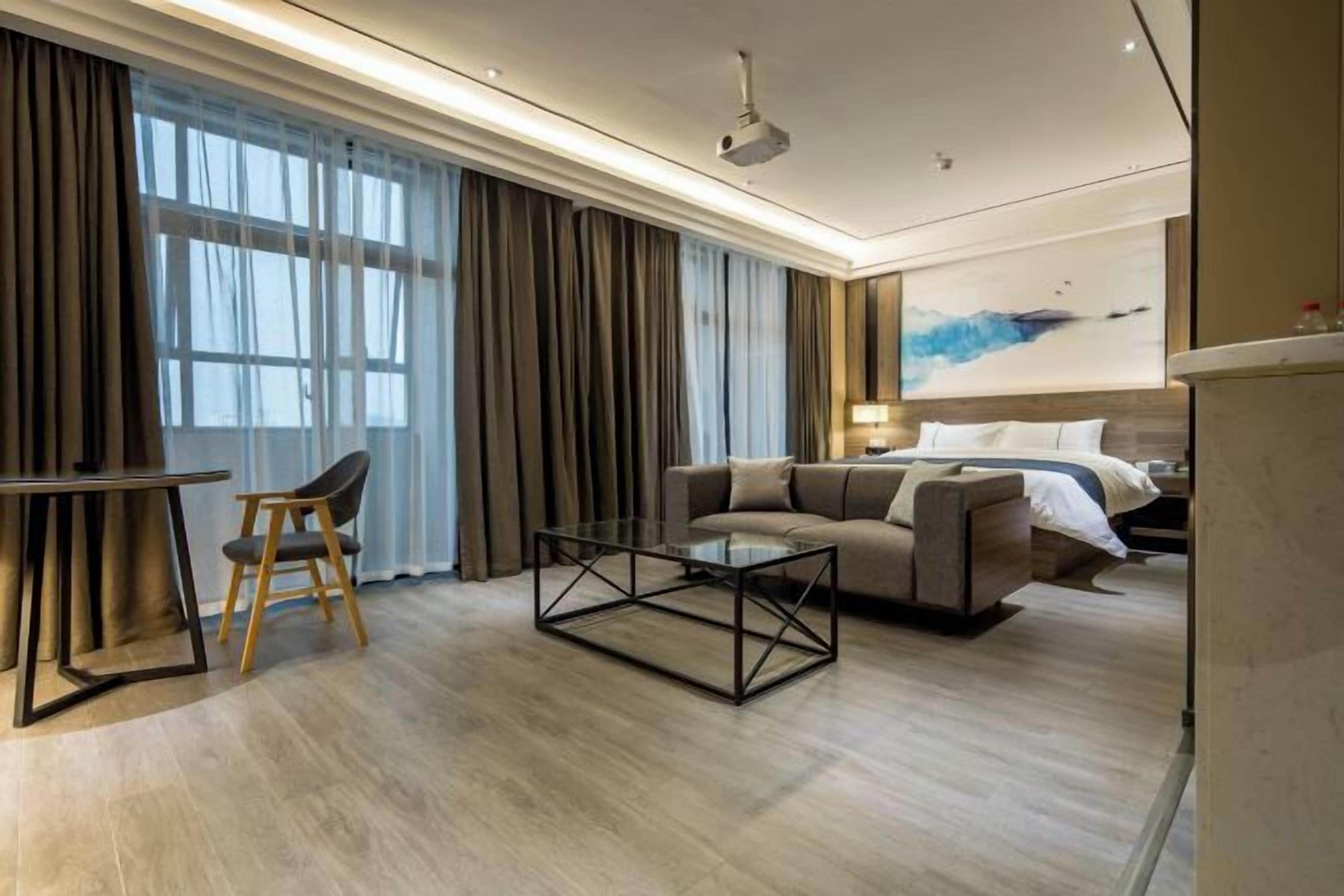 Habitación de hotel moderna con sofá, mesa de centro, zona de comedor con una silla y cama con cabecero.