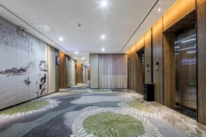 A hotel corridor with patterned carpet, wooden walls, and an elevator.