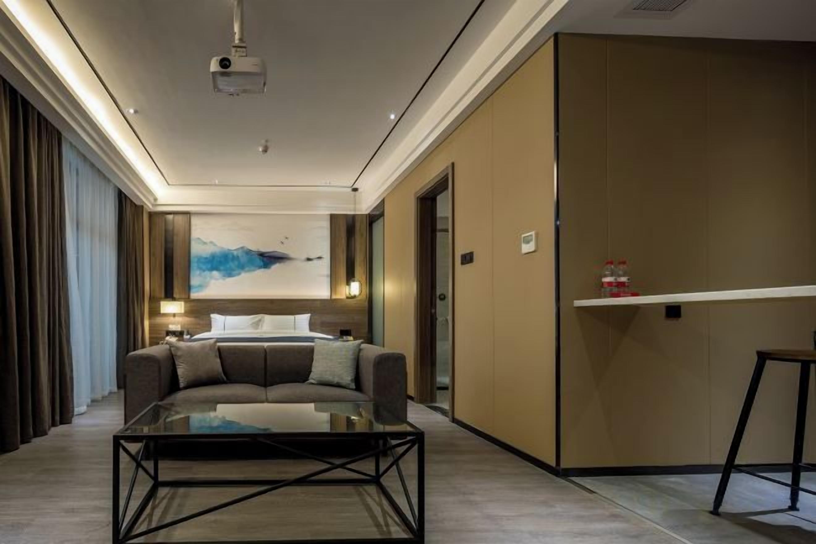 A modern hotel room with a sofa, a glass coffee table, a painting on the wall, and a door leading to another room.