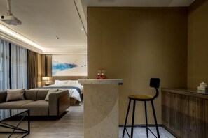 A hotel room with a bed, a seating area, a bar, and a large painting on the wall.