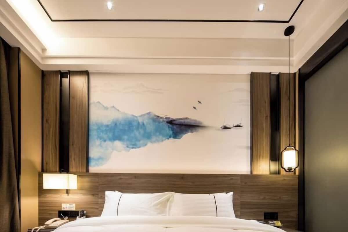 A hotel room with a large bed, wooden paneling, a wall-mounted lamp, and a painting of mountains and birds.