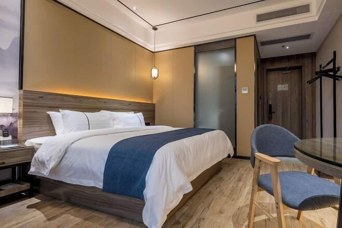 A modern hotel room with a bed, bedside table, chair, and a glass table.