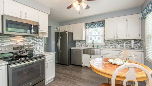 A modern kitchen with stainless steel appliances, white cabinets, and a wooden dining table. - Central Tosa home near downtown, state fair, froedtert (Wauwatosa)