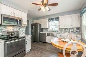Una cocina moderna con electrodomésticos de acero inoxidable, armarios blancos y una mesa de comedor de madera.