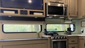 Cocina compacta con televisor de pantalla plana, microondas, estufa, horno y chimenea empotrada.