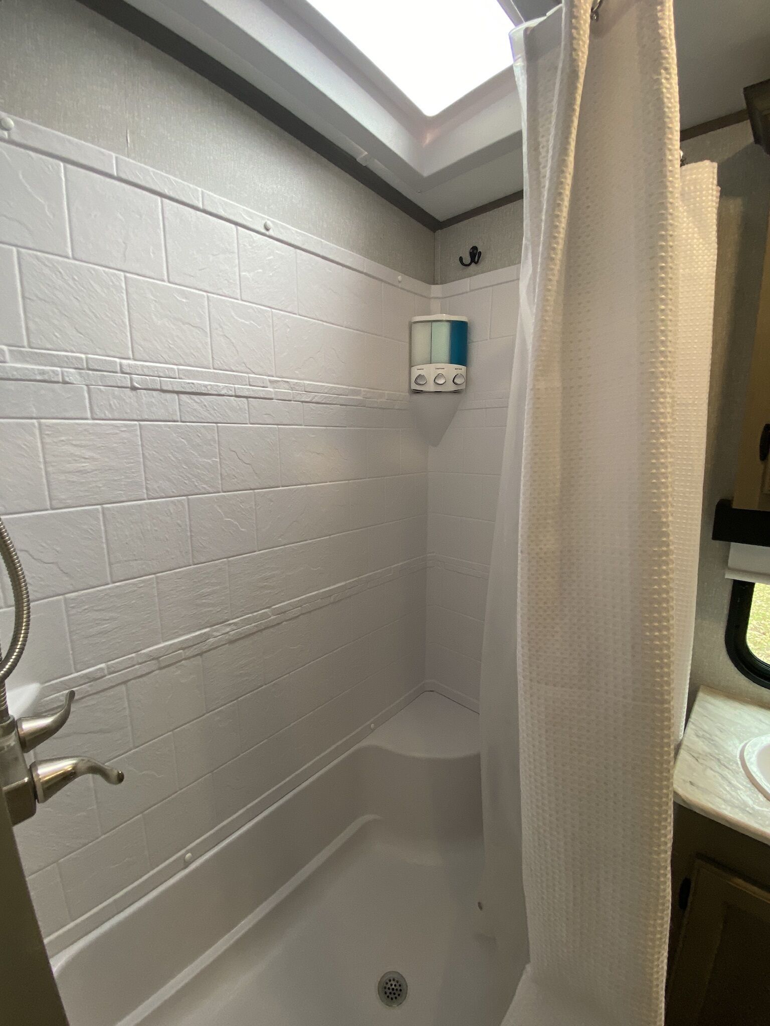 Une douche avec des carreaux blancs, un distributeur de savon et un rideau de douche.