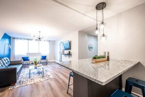 Un salon moderne doté d’un grand îlot central, d’un ventilateur de plafond et d’un téléviseur fixé au mur.