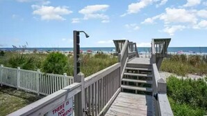A wooden boardwalk leading to beach umbrellas and a lifeguard tower. - Oceanfront Getaway,  Directly on the Beach with Amazing Views (Surfside Beach)