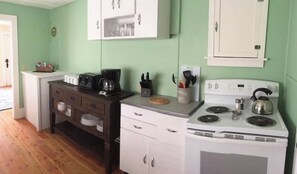 A compact kitchen with white cabinets, a stove, and a coffee maker.