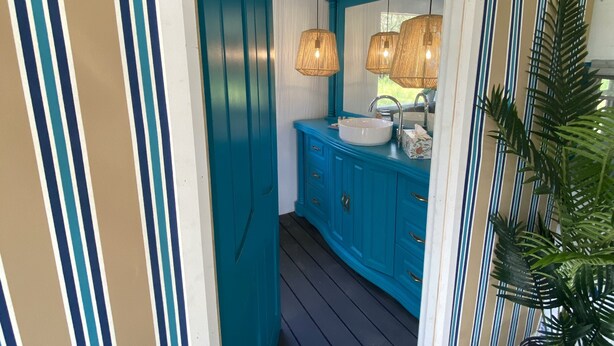 A narrow hallway with teal and white striped walls, a wooden door, and a sink area with a mirror and hanging lights. - 'Alice' Crescent Head's coolest retro caravan (Crescent Head)