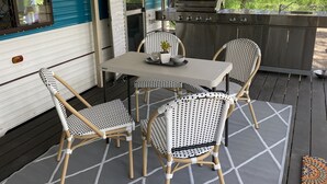 A covered outdoor patio with a table and chairs, a grill, and a window overlooking greenery. - 'Alice' Crescent Head's coolest retro caravan (Crescent Head)