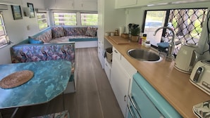 A compact kitchen with a sink, stove, and seating area. - 'Alice' Crescent Head's coolest retro caravan (Crescent Head)
