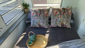A cozy interior with a bed, pillows, a tray with a teapot and cup, and a window with blinds. - 'Alice' Crescent Head's coolest retro caravan (Crescent Head)