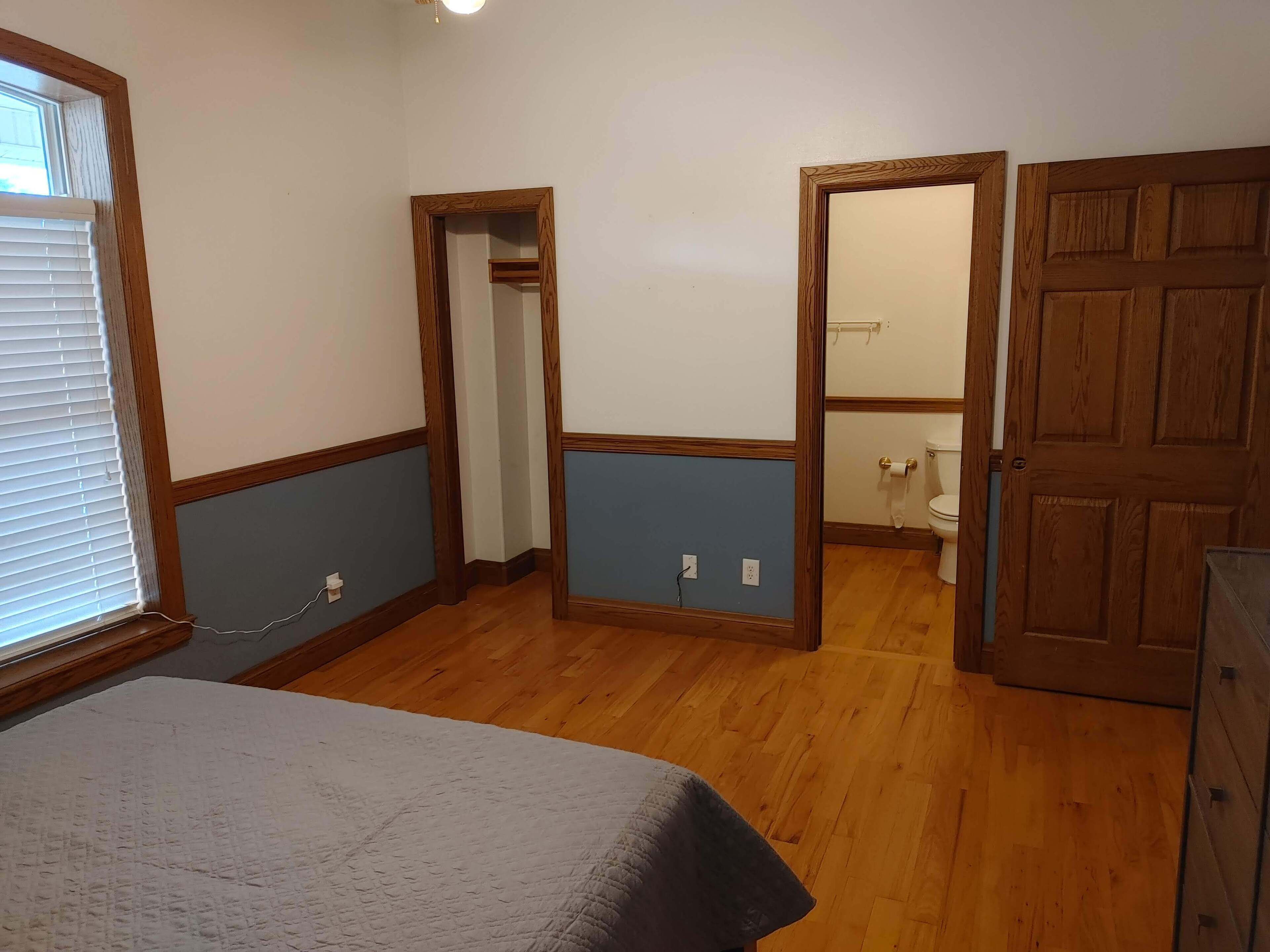 A bedroom with a bed, wooden door, and a bathroom visible through an open door.