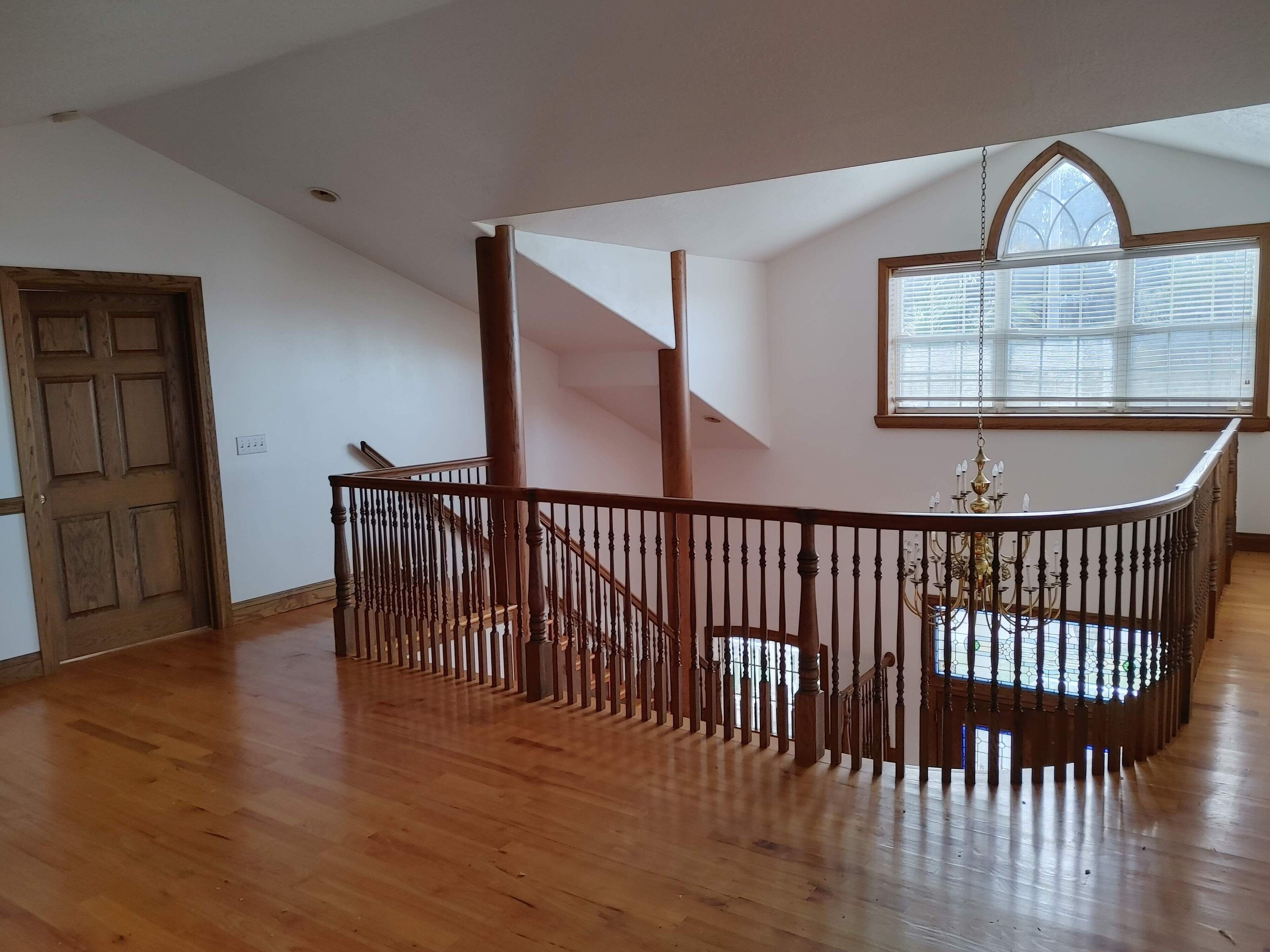 Una habitación amplia con escalera de madera y un gran ventanal con persianas.