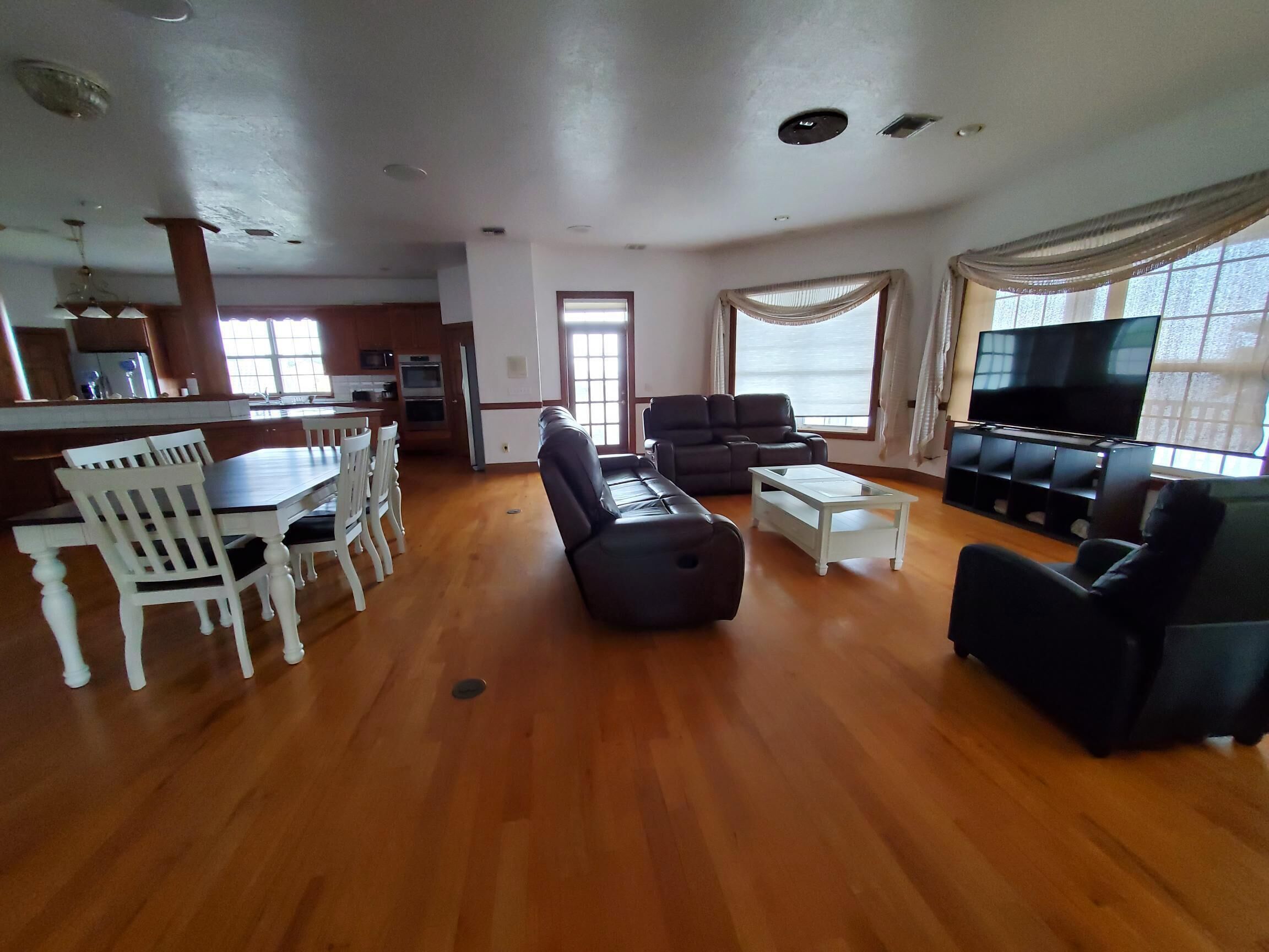 A spacious living room with a dining area, a sofa, a TV, and a kitchen in the background.
