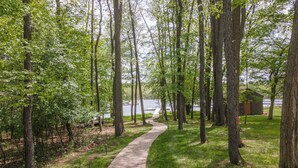 A paved pathway through a wooded area with a small cabin in the background. - Cozy Dog Friendly, Private Dock & Fire Pit (Oakland)