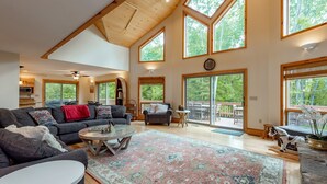 A spacious living room with a large rug, a sofa, a coffee table, and a fireplace. There are large windows allowing natural light and views of the outdoors. - Cozy Dog Friendly, Private Dock & Fire Pit (Oakland)
