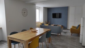 Ein modernes Wohnzimmer mit einem Holzesstisch, bunten Stühlen, einer Couch und einer Wand mit Muster.