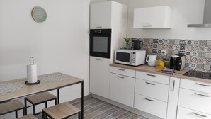 Eine kompakte Küche mit Mikrowelle, Toaster und Kaffeemaschine. Ein kleiner Tisch mit Papiertuchhalter und einer Pflanze steht auf der Arbeitsfläche.