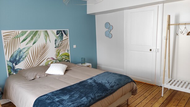 Ein Schlafzimmer mit einem Bett, einem Kopfteil mit tropischem Blattmuster, einer weißen Tür und einem Holzboden.
