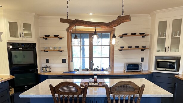 A kitchen with a large island, two wooden bar stools, a hanging light fixture, and built-in appliances.