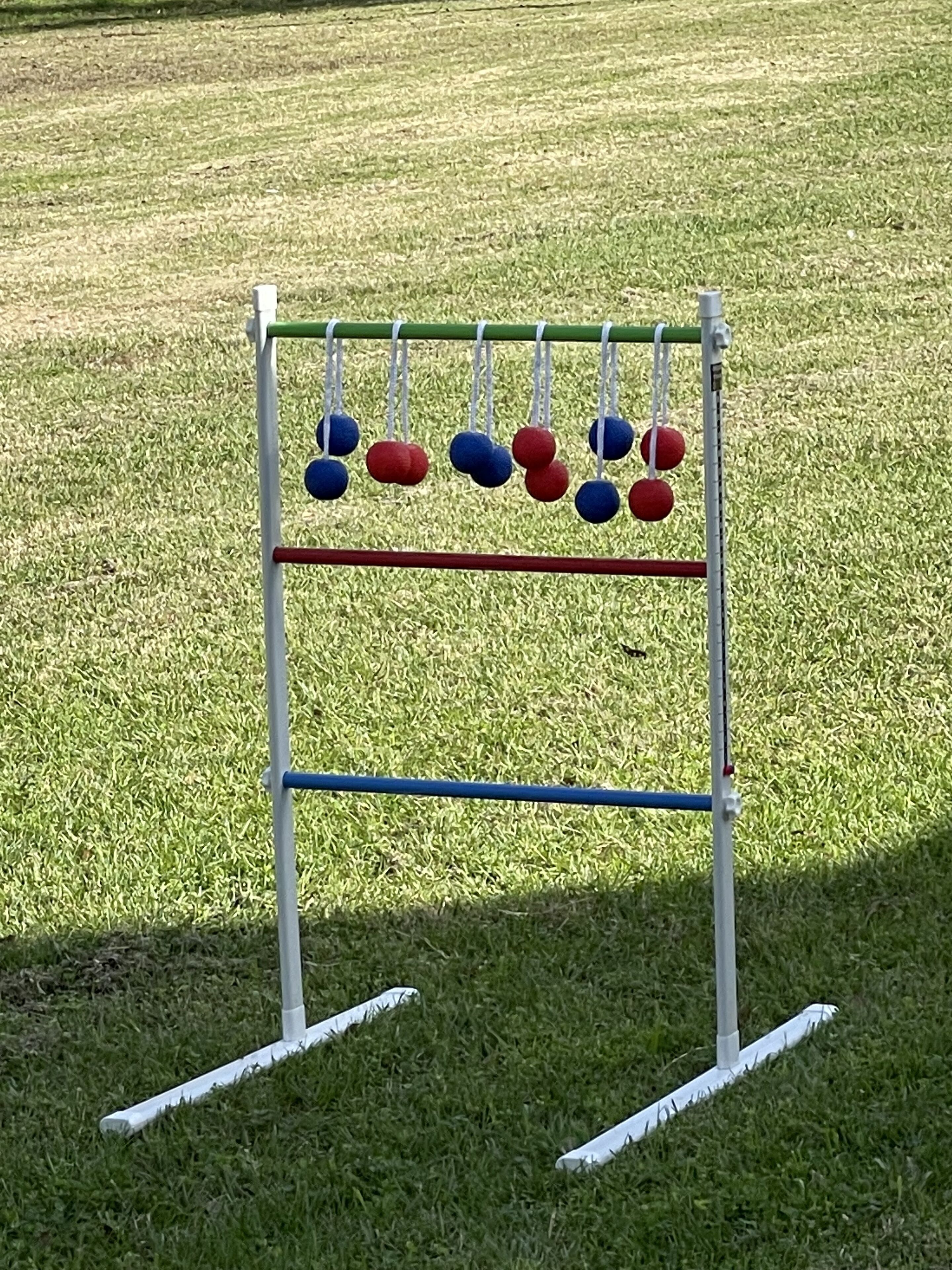 A game board with red and blue balls hanging from a white frame, set on a grassy field.