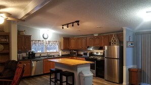 Una cocina moderna con armarios de madera, electrodomésticos de acero inoxidable, una isla central con taburetes y un reloj en la pared.