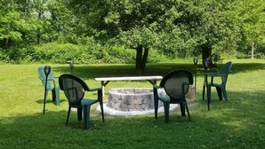 Un patio con una mesa redonda y cuatro sillas, rodeado de césped y árboles.
