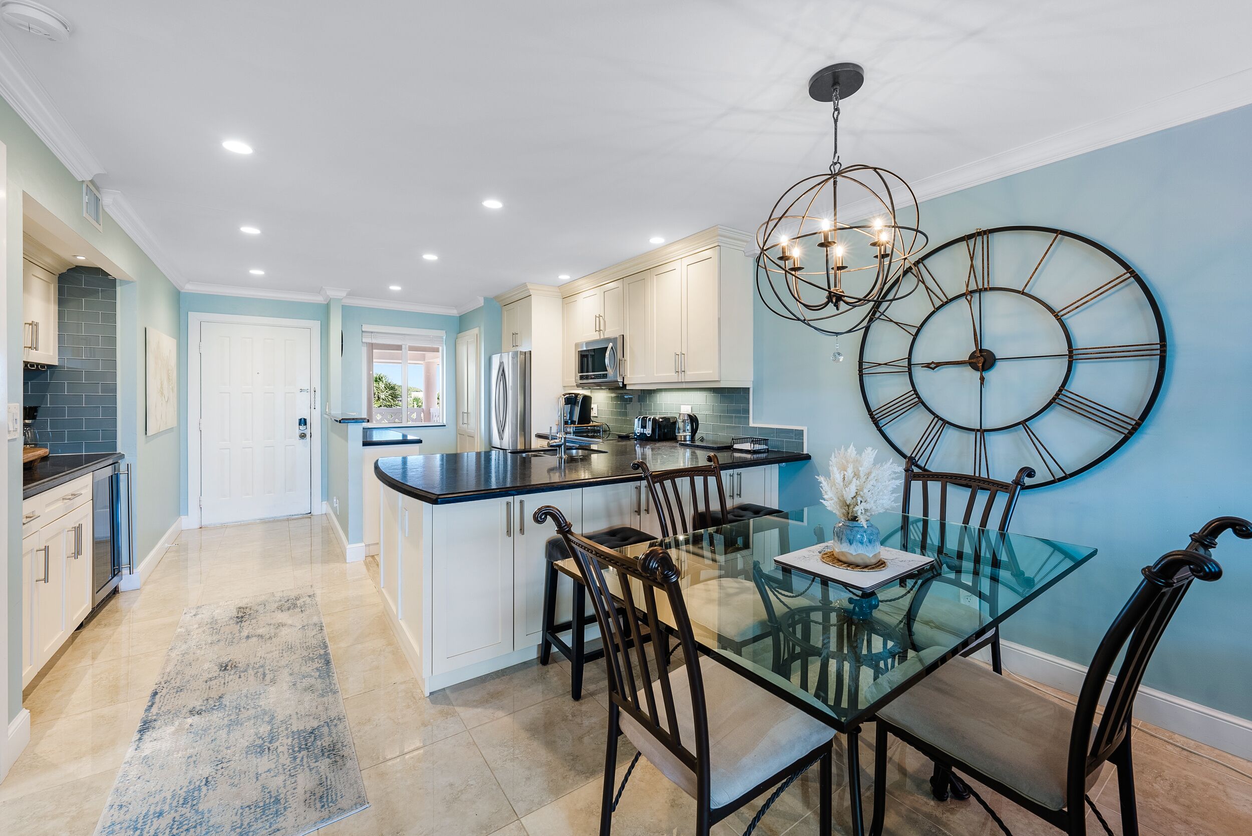 A modern kitchen with white cabinets, a glass island, and a large wall clock.