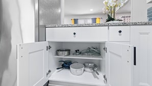 Una cucina con mobili bianchi, un piano di lavoro in granito e diversi utensili da cucina, tra cui pentole e padelle.