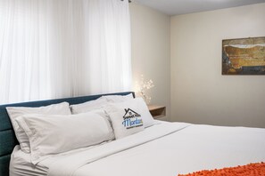 A neatly made bed with white linens and a pillow featuring a logo. - Bison at Buffalo Jump (West Yellowstone)