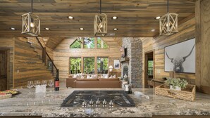 A spacious kitchen with a large island, wooden walls, and a stone fireplace. - Luxury Forest Escape with Charm - Hot Tub, Game Loft, Pool Table and Playground (Broken Bow)