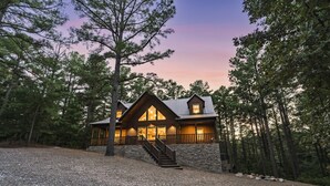 A lodge with a stone exterior, a wooden deck, and a staircase leading to the entrance. - Luxury Forest Escape with Charm - Hot Tub, Game Loft, Pool Table and Playground (Broken Bow)